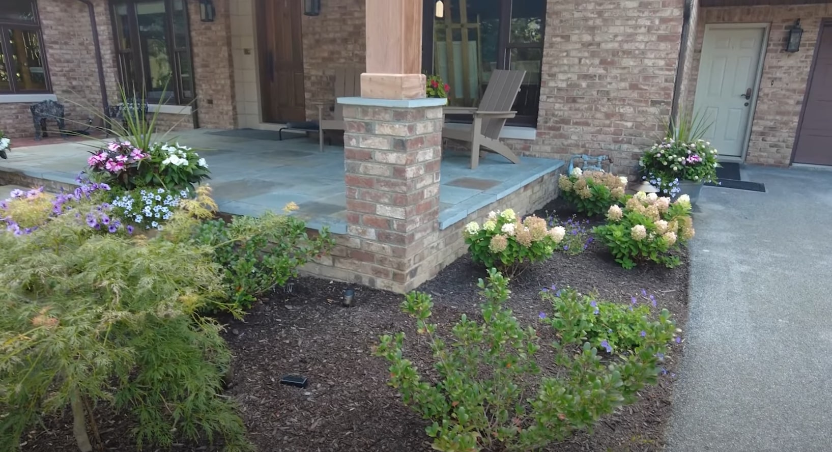 Contemporary outdoor living area with brick hardscaping and colorful seasonal plantings Modern residential outdoor living space with brick columns and professional landscape design